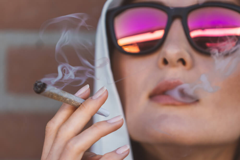 a person in a hoodie and sunglasses enjoying a marijuana pre roll