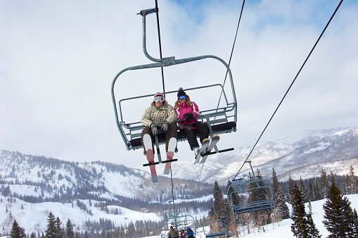 two people sitting on a chair lift going up the mountain